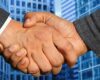 Zoomed photo of hands shaking against a background of business buildings